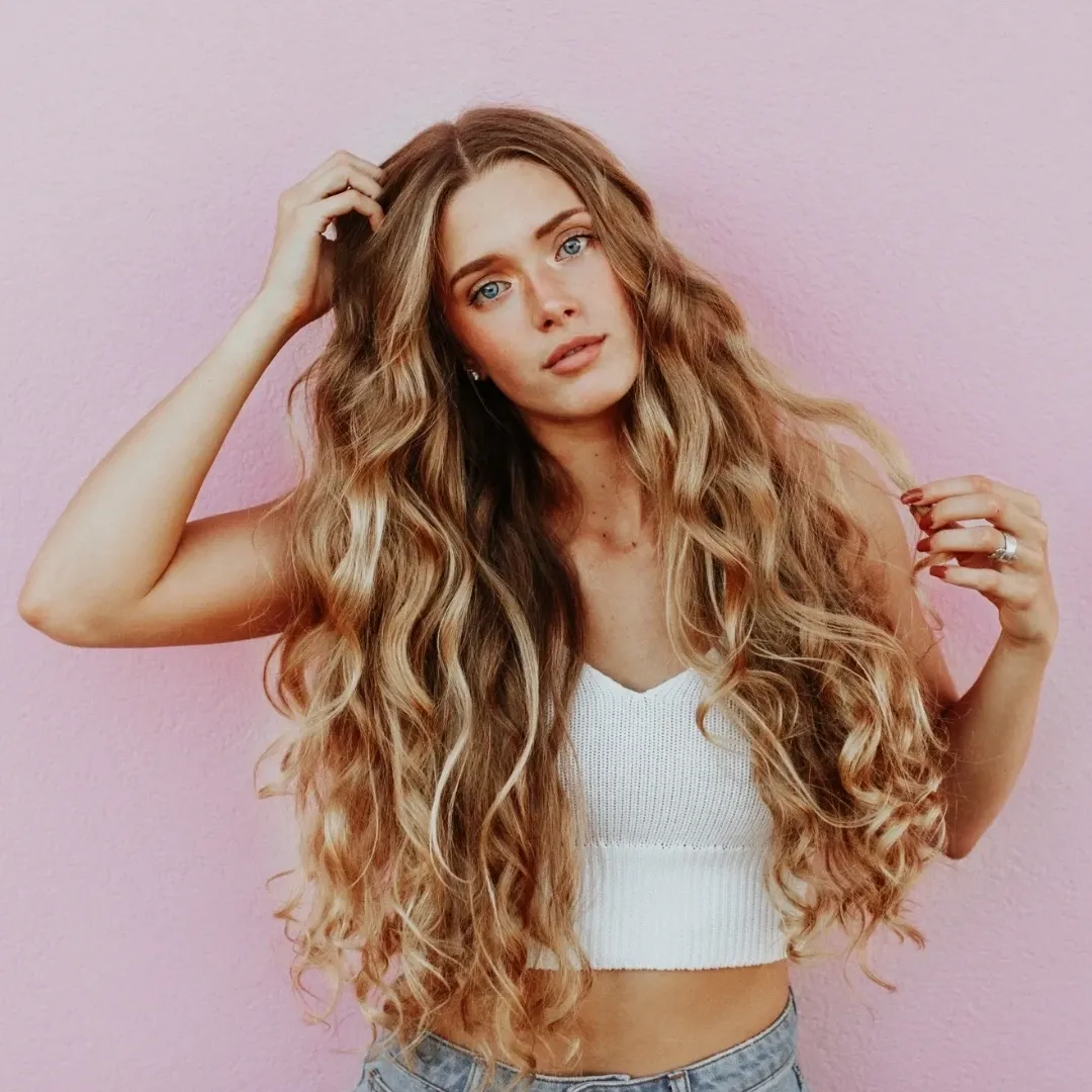 Hair Haven Extension Academy A woman with long hair is standing against a pink wall.